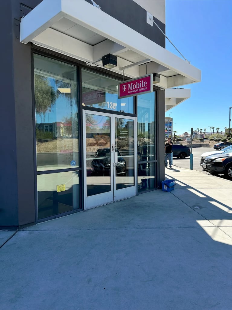 Exterior view of a T-Mobile store with glass doors and storefront signage in a shopping area with clear sky