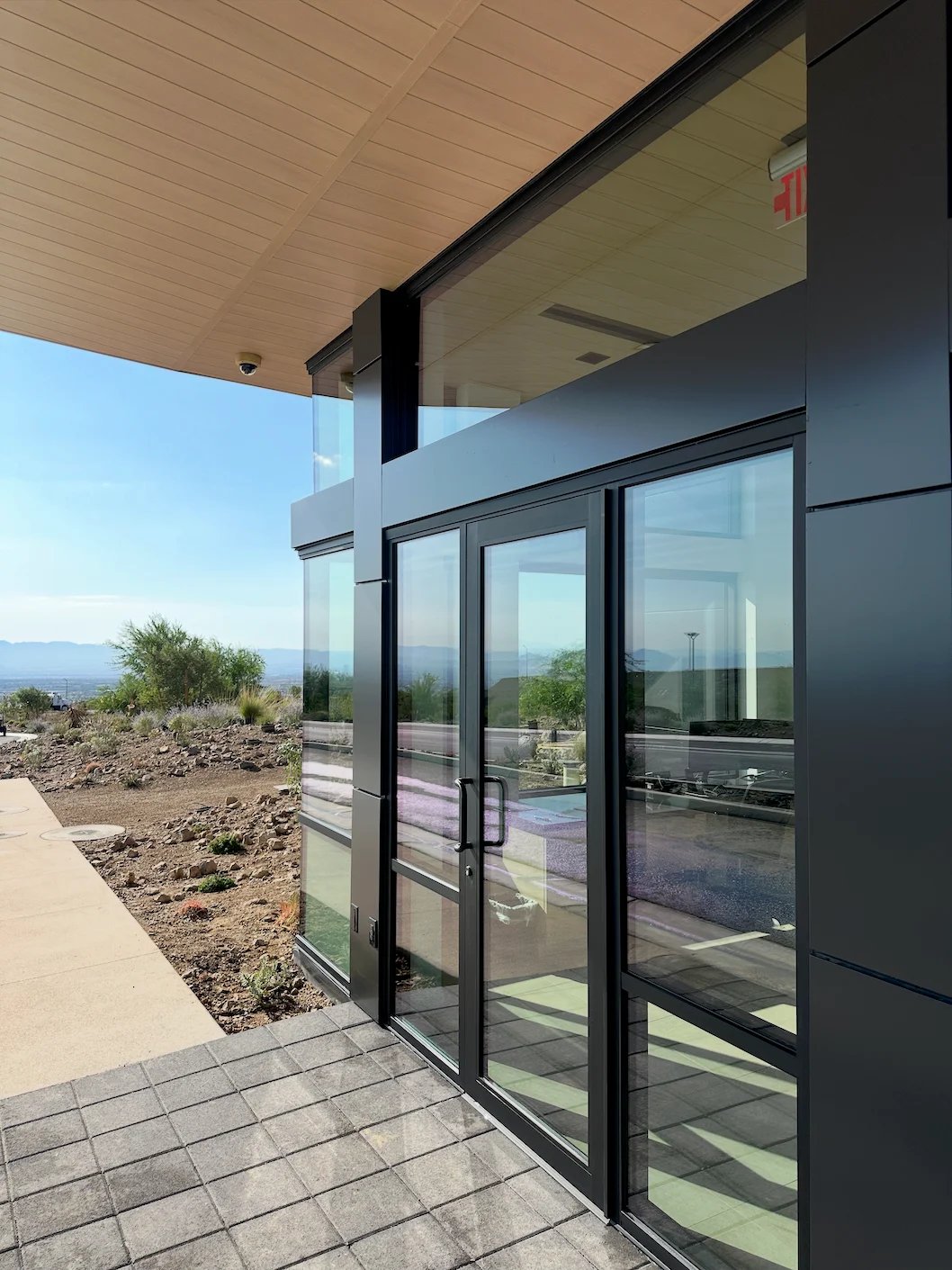 Modern home exterior with black-framed sliding glass doors, concrete patio, and desert landscape view with mountains in distance