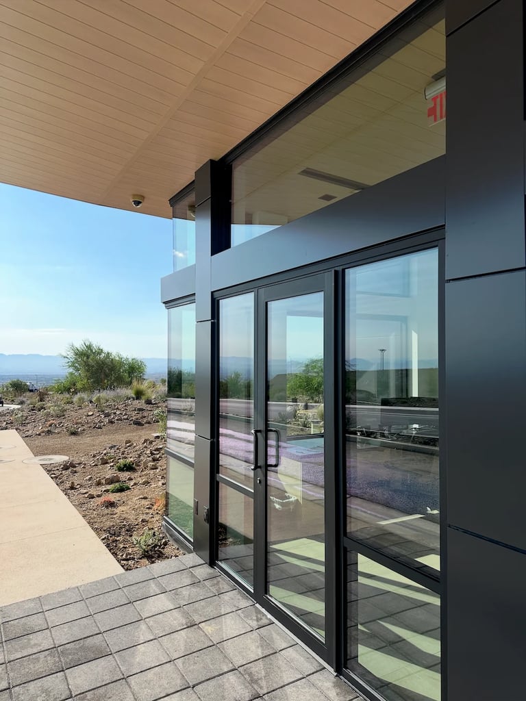 Modern home exterior with black frame glass sliding doors, wooden ceiling overhang, and desert mountain landscape views